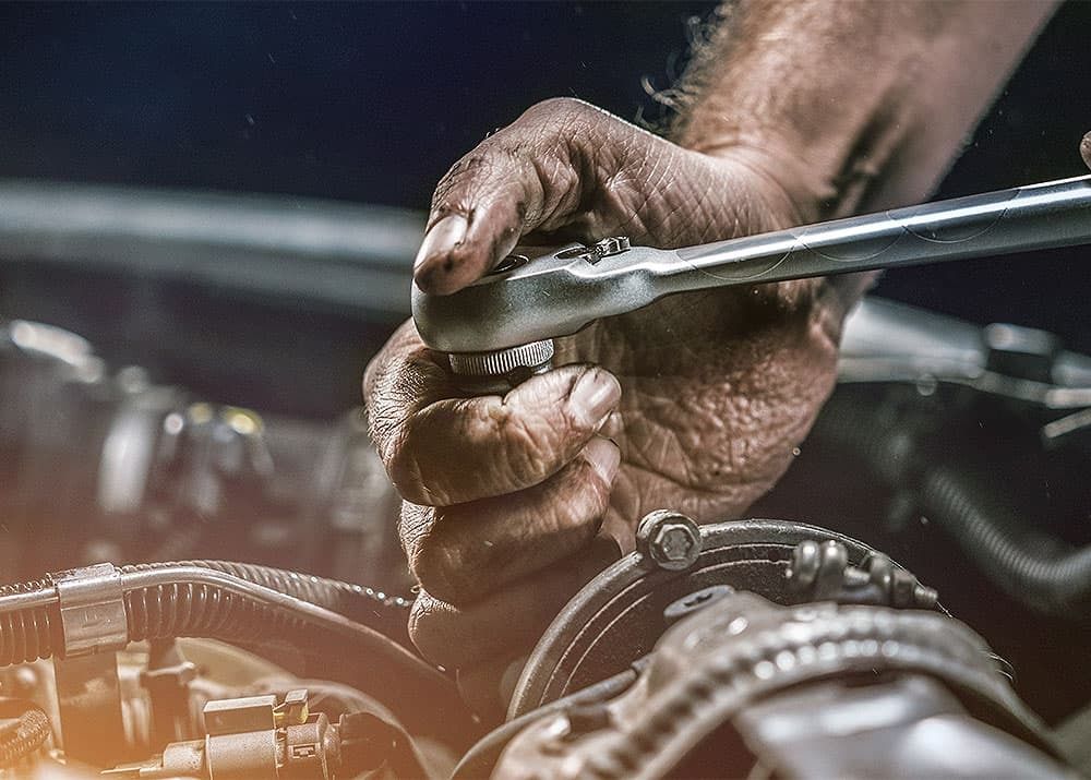 Die Hand eines Mannes werkelt am Motor eines Autos